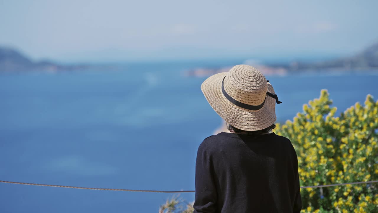 希腊暑假，戴着帽子的年轻女子站在悬崖上，俯瞰苏尼翁角的全景。时尚女黑头戴帽，电影式的孤立镜头视频素材