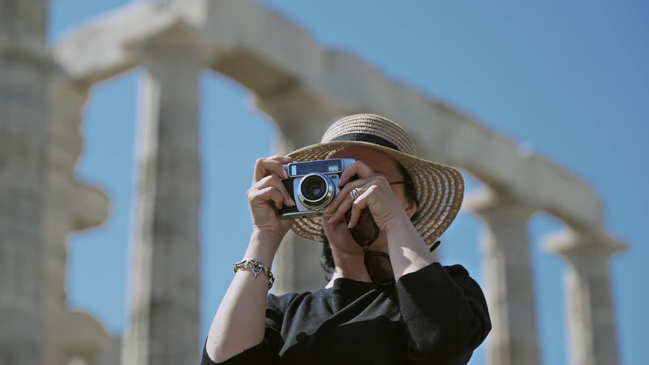 在希腊雅典附近的苏尼翁，一名女游客正在用复古相机拍摄波塞冬神庙遗址视频下载
