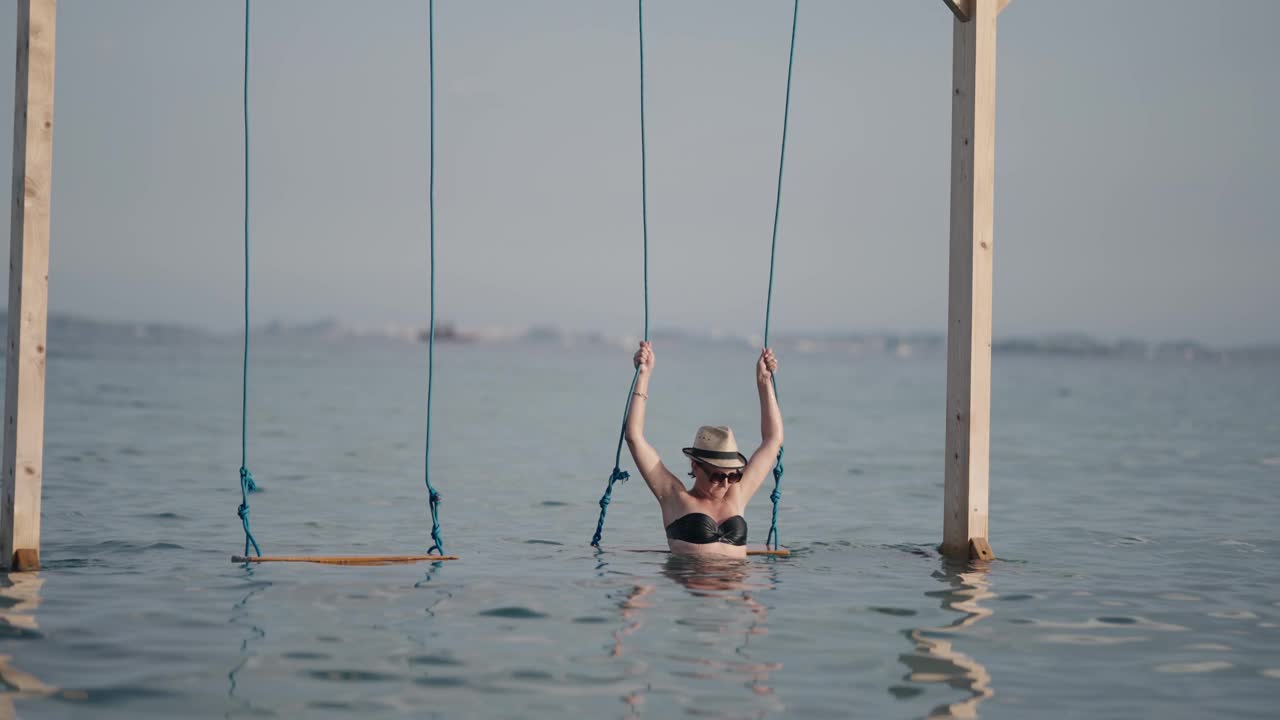 旅行者的女人有乐趣的绳秋千以上的海水在沙滩上的慢动作，暑假的概念视频下载