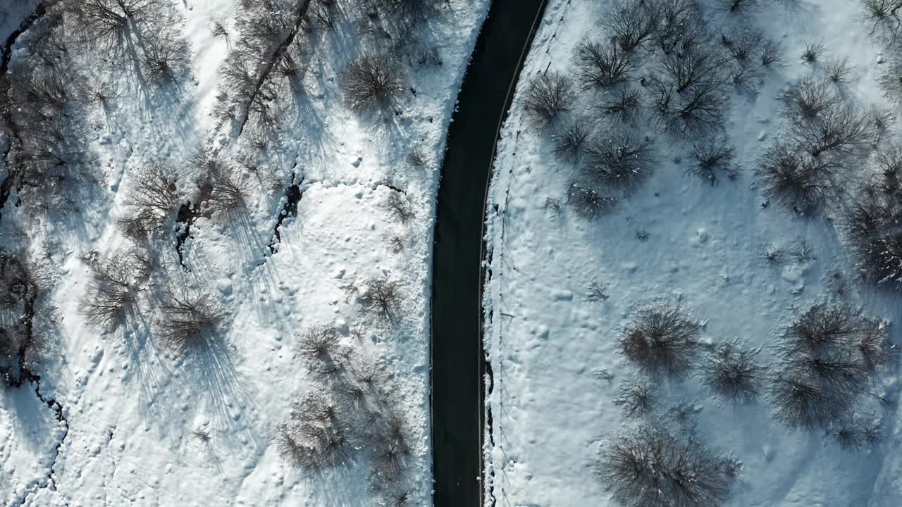 鸟瞰白雪覆盖的风景，一条蜿蜒的道路穿过光秃秃的树木视频素材