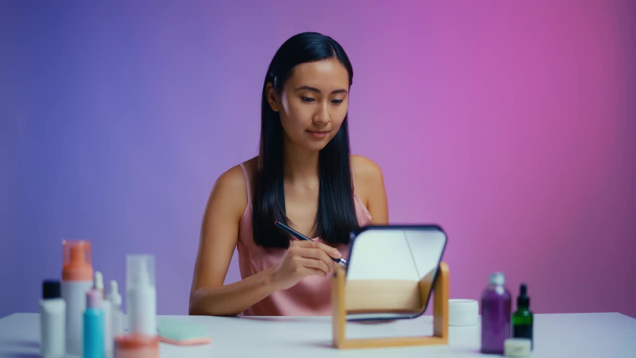 亚洲女性在镜子前涂粉，化妆，美容程序视频下载