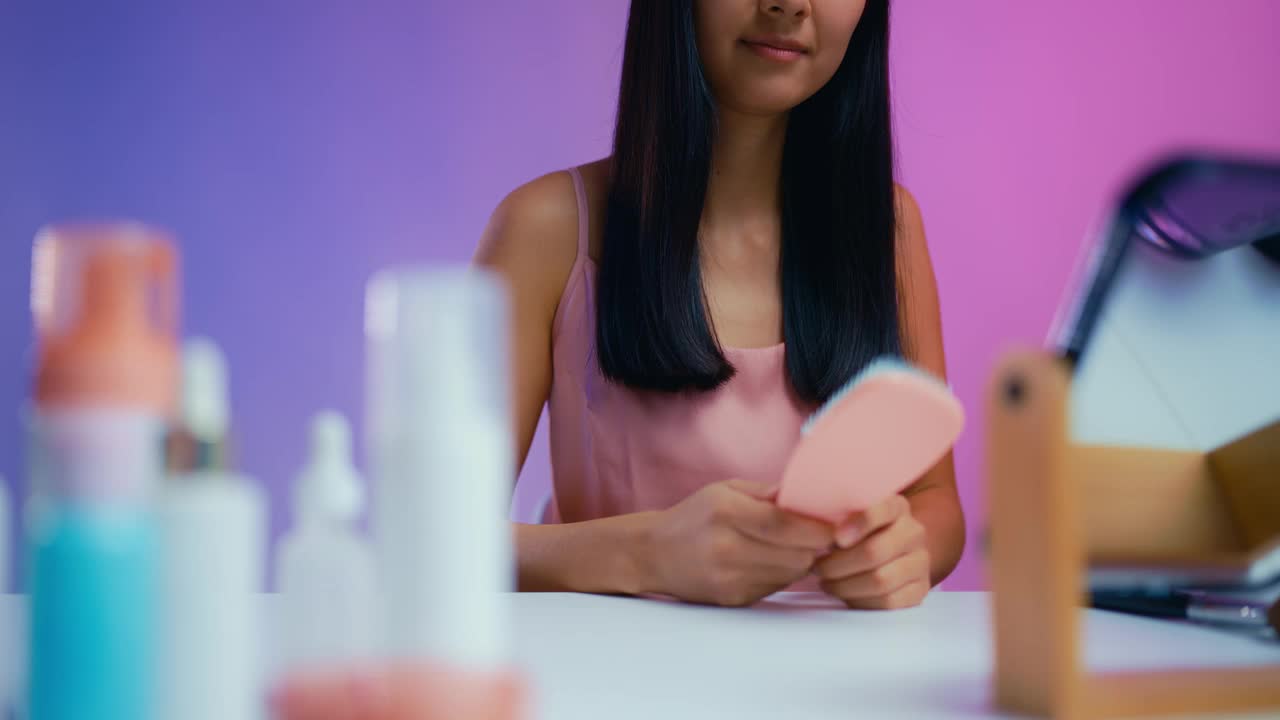 微笑的亚洲妇女在镜子前梳理她健康的头发，护发产品视频下载