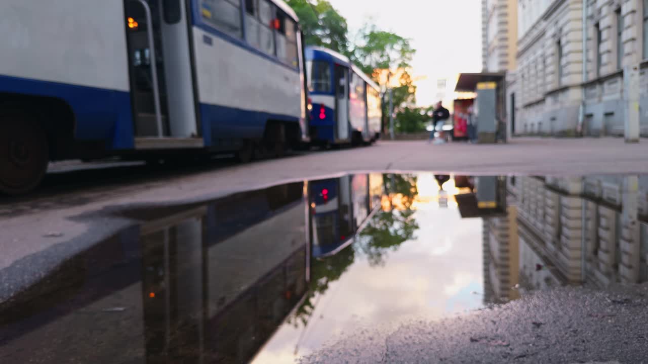 这张照片展示了雨后城市街道水坑上公交车的倒影，周围是城市基础设施和建筑视频素材