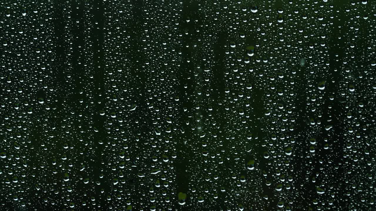 雨滴落在玻璃上的特写视频。深黑色背景。纯净和新鲜。视频素材