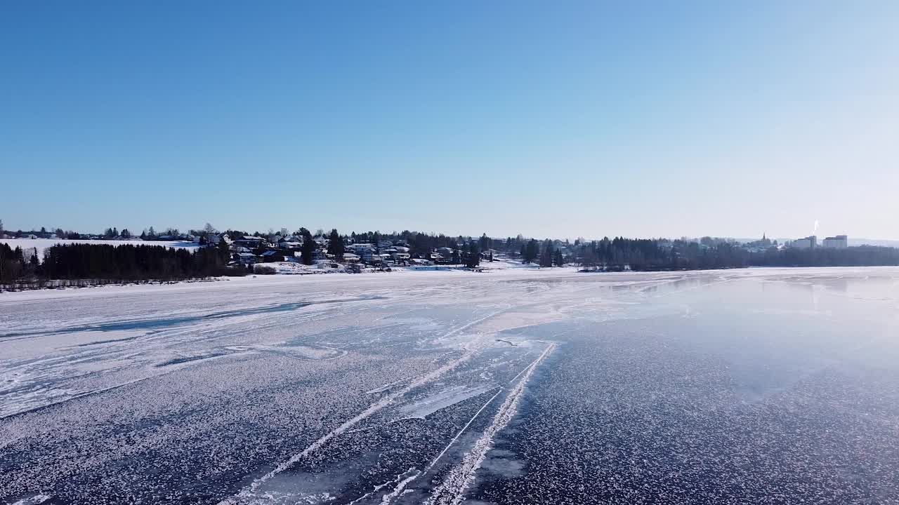 挪威一个冰冻的湖泊的宁静景色，在晴朗的蓝天下，白雪覆盖的房屋和树木成为背景。视频素材