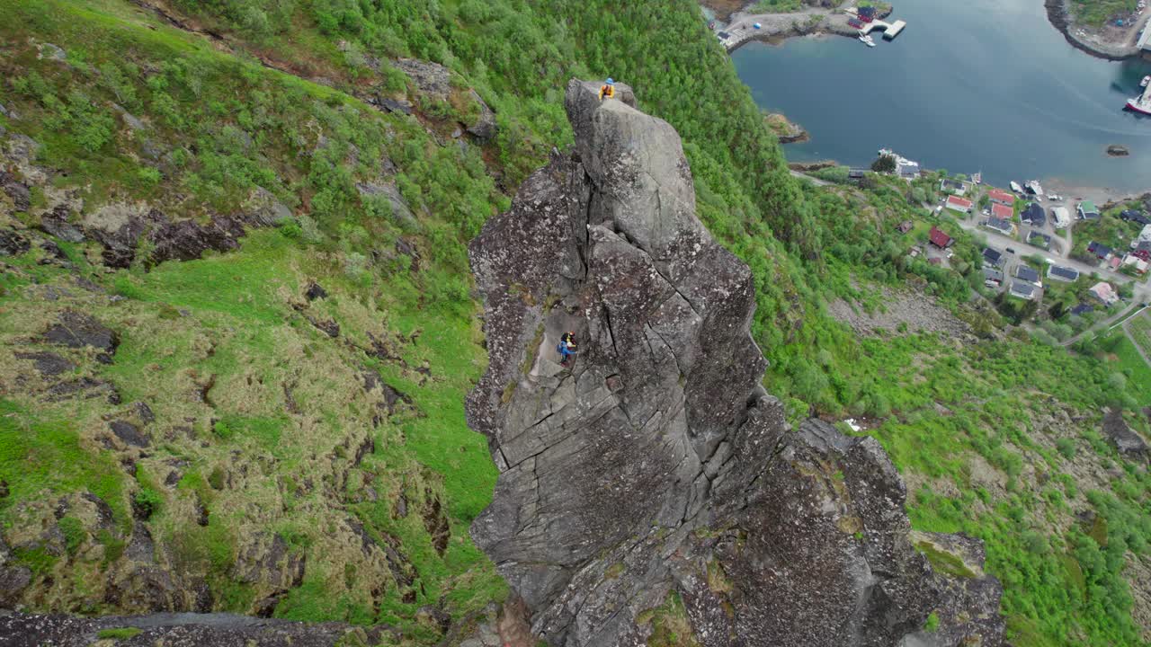 电影鸟瞰图，一个穿着黄色衣服的登山者在春天的Svolvaergeita(山羊)岩石顶峰的顶部。敦,挪威。视频素材