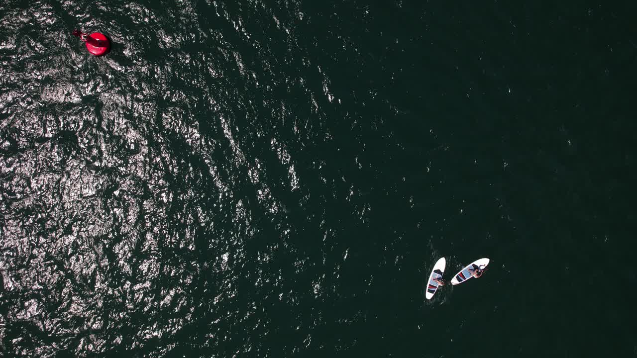 两个人站起来的鸟瞰图，在波涛汹涌的海面上，在一个红色的灯塔旁边登船。摄于葡萄牙卡斯凯伊斯视频下载