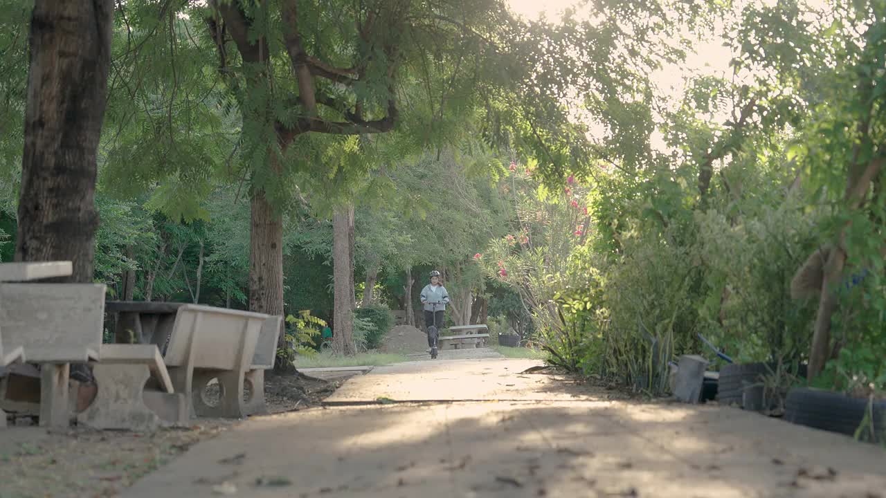 夏日阳光明媚的一天，一名亚洲女子在公园里骑着电动滑板车。视频素材