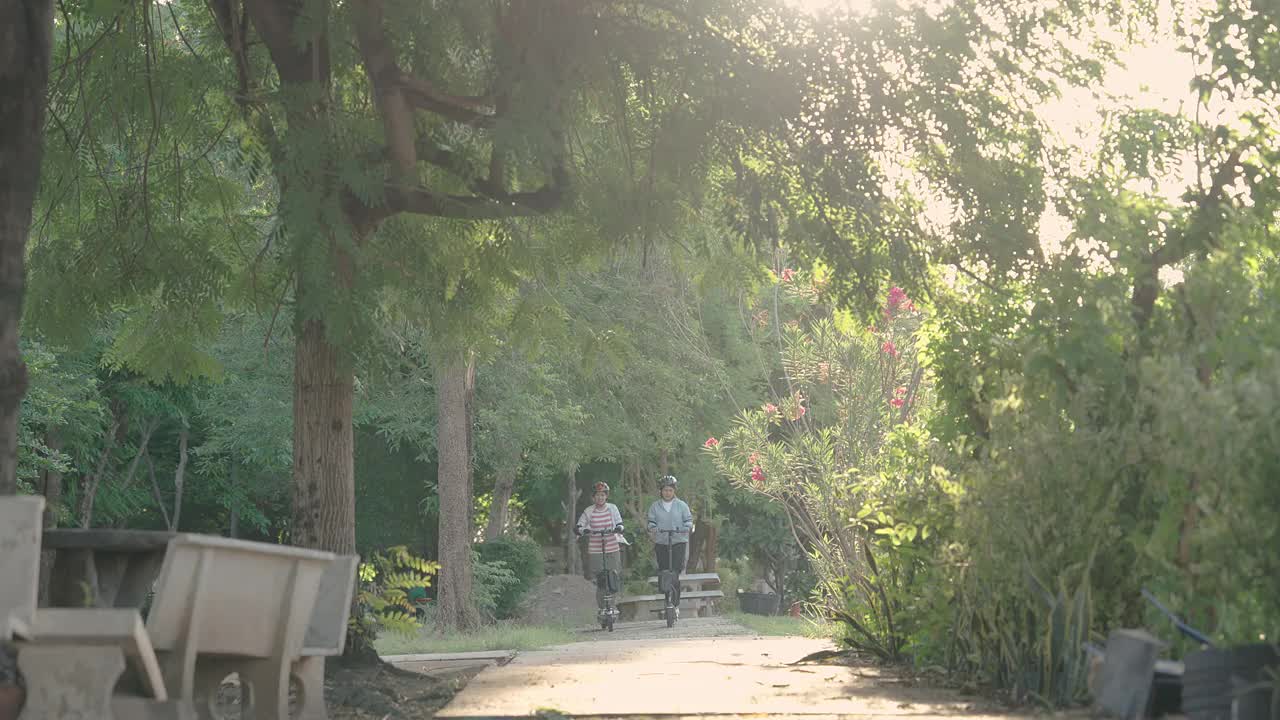 两个年轻的亚洲女子在公园里骑着电动滑板车。视频素材