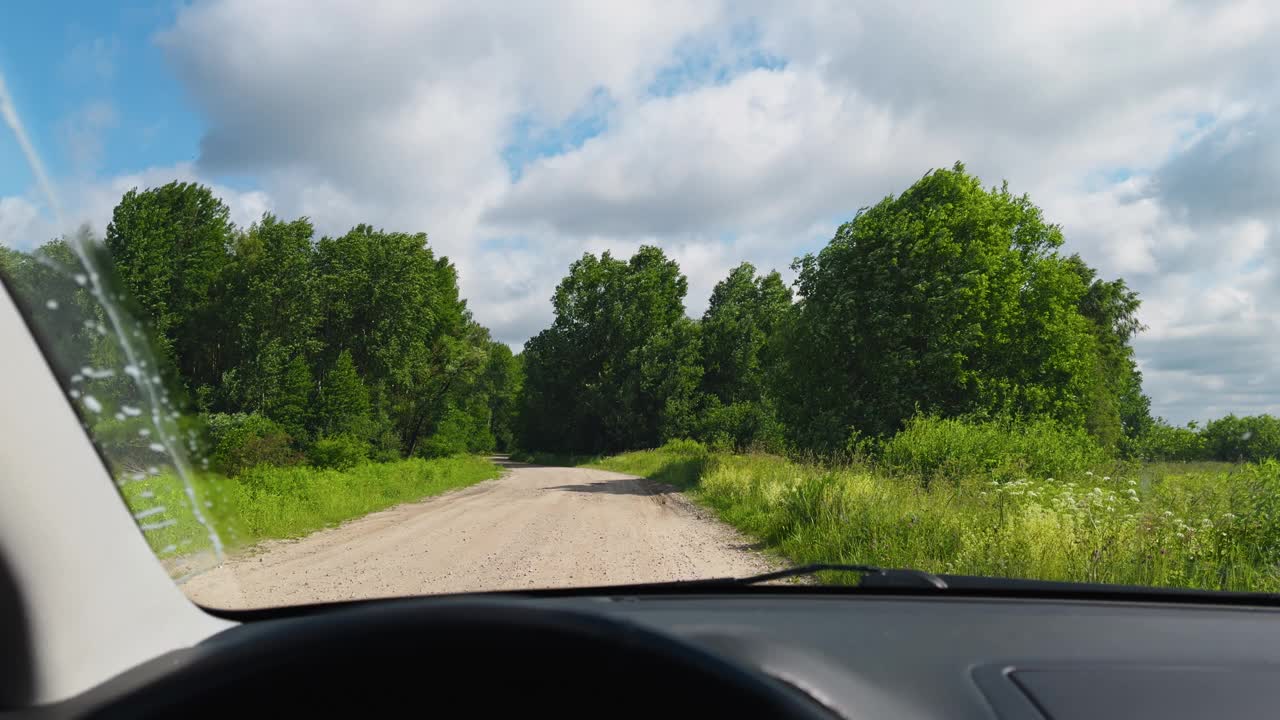 POV挡风玻璃视图:一个人在夏天开车在乡村道路上，绿色的树木和蓝天为背景视频素材