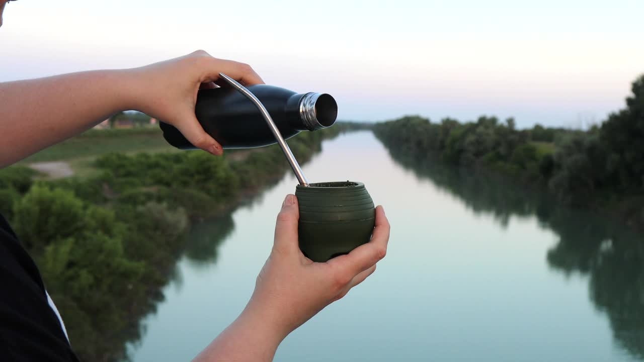 女性的手把马黛茶从热水瓶里倒进硅胶马黛茶葫芦里视频下载