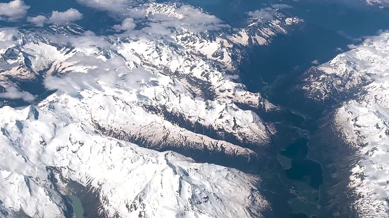 从飞机窗口看到的美景。镜头的场景看着窗外，看到美丽的阿尔卑斯山上的山脉，飞过天空的云。旅游及交通概念视频素材