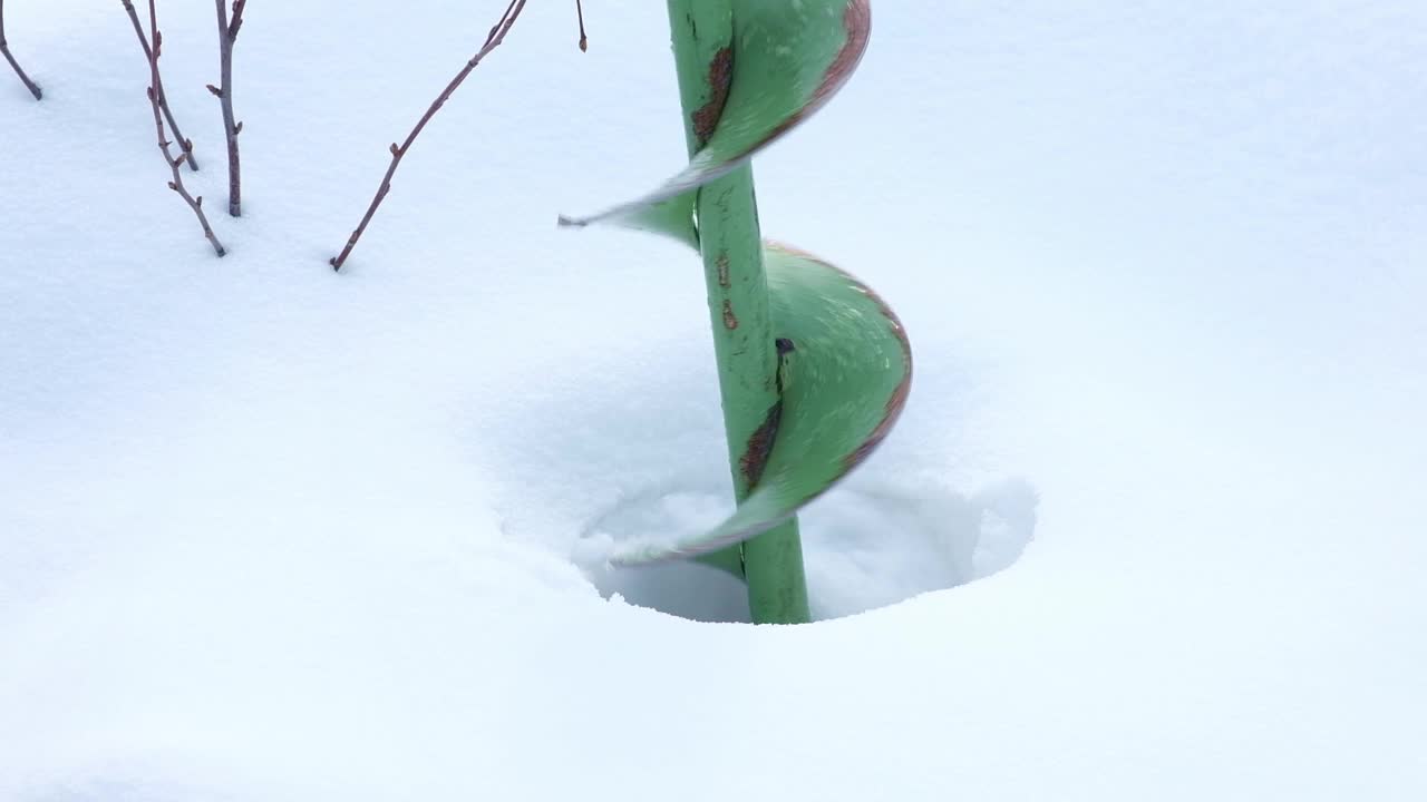 绿色手工冰钻钻入冰雪覆盖的冰面，创造一个钓鱼洞在冬季景观视频下载