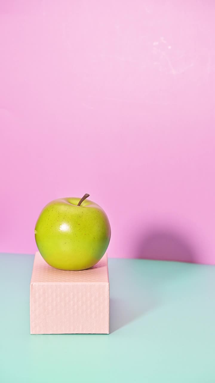 绿色的苹果欢快地跳跃在粉红色的盒子上。垂直止动视频素材