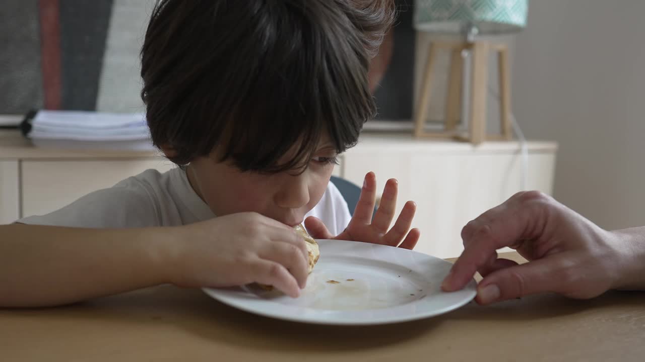 小男孩热情地咬了一口煎饼，带着喜悦的表情品尝着味道，在餐桌上捕捉到了一个坦率而愉快的时刻视频素材