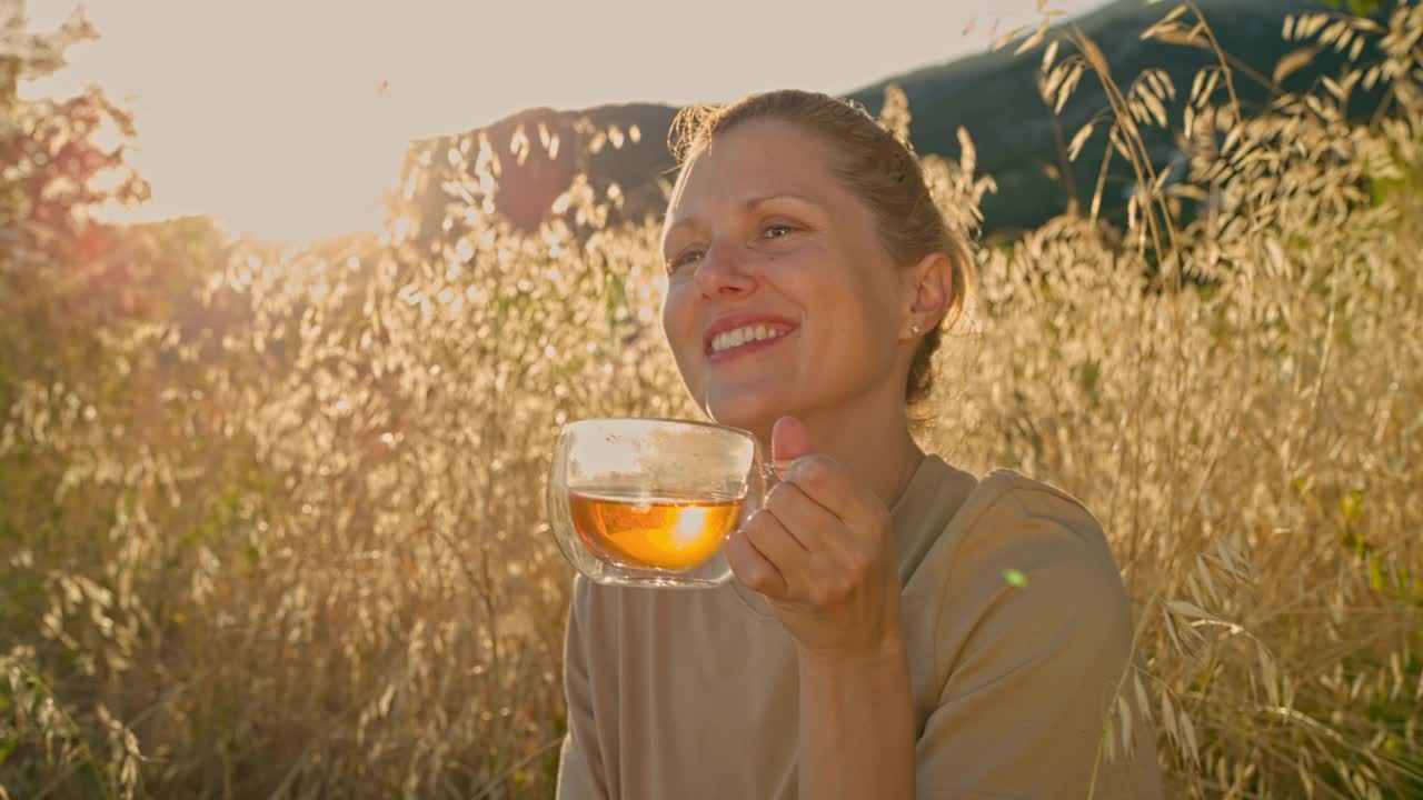 日落时分，一位妇女在野餐中享受着一杯茶。视频素材