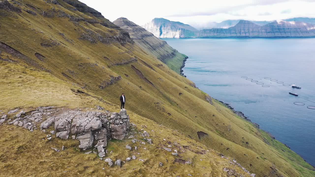 在法罗群岛的福宁古尔山顶上绕着一个徒步旅行者飞行视频素材