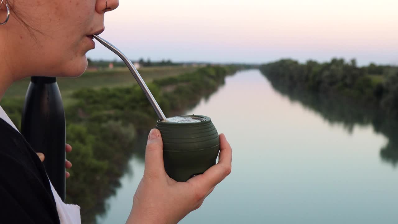 一个女人用硅胶罐喝马黛茶。户外景观为背景视频下载