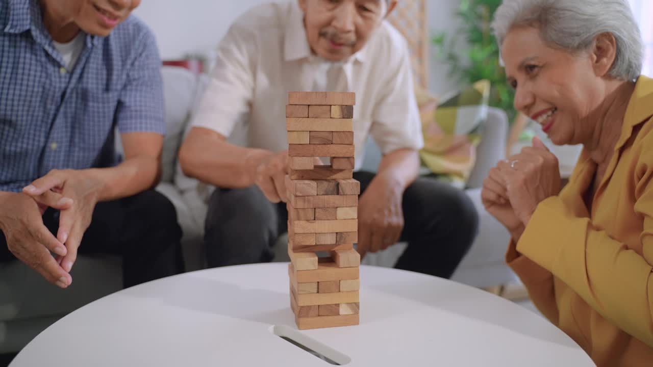 一群高年级的朋友在家里的客厅里玩积木游戏。亚洲成熟的老年男女感到快乐和放松，花时间玩棋盘游戏，从一堆木砖中拉。视频素材