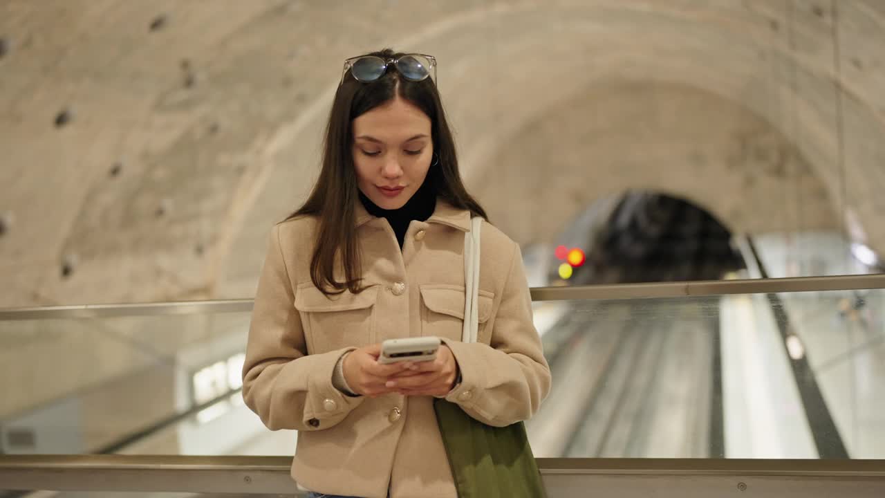 年轻的黑发女子在地铁站用智能手机发短信视频素材