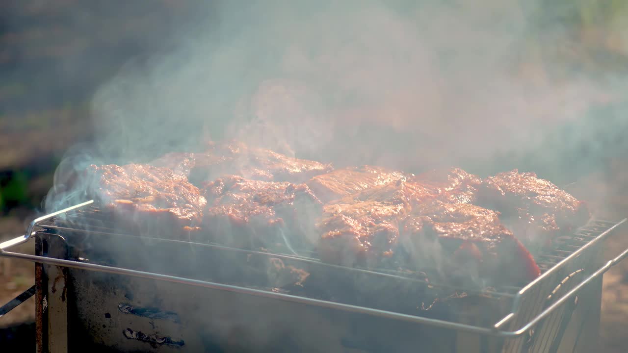 在烤肉架上烤肉。在背光照射下，在明火上烤肉时，烟雾和蒸汽从上方升起视频素材