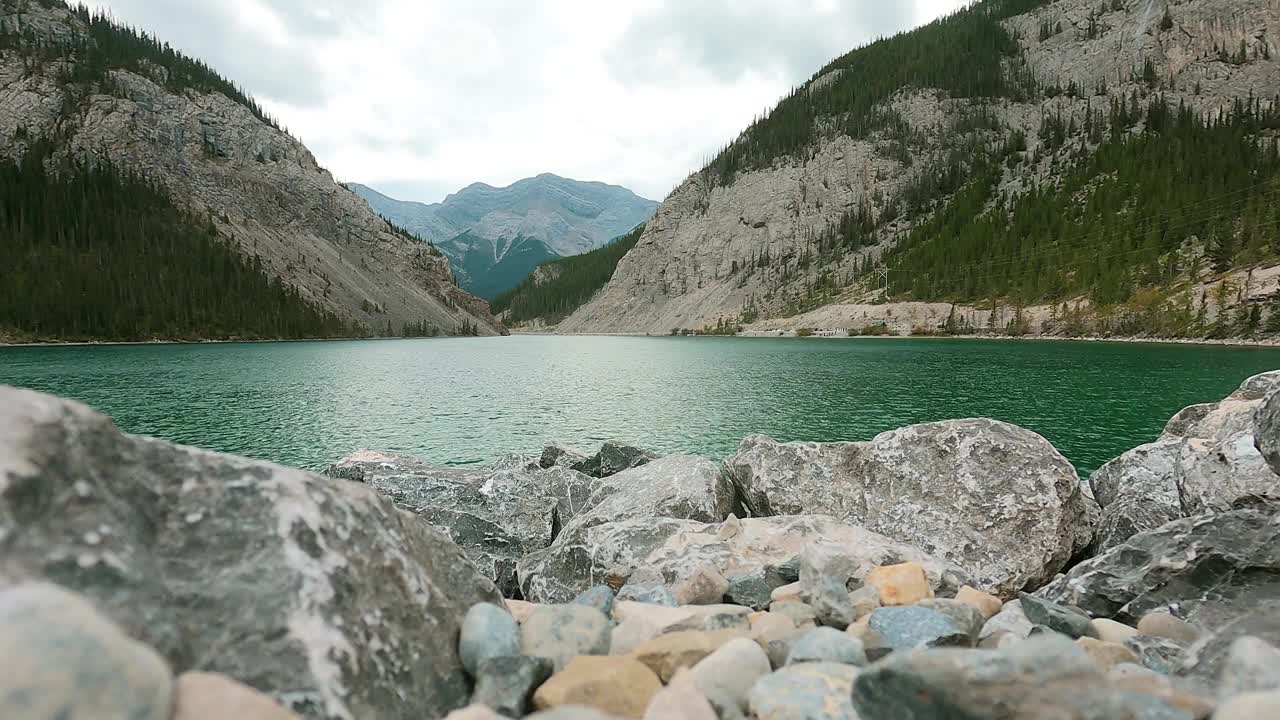 淡水湖与落基山脉的自然背景。站在一个阳光明媚的日子里。绿色的水面在柔和的风吹下轻轻移动，为风景营造出轻松的质感。视频下载