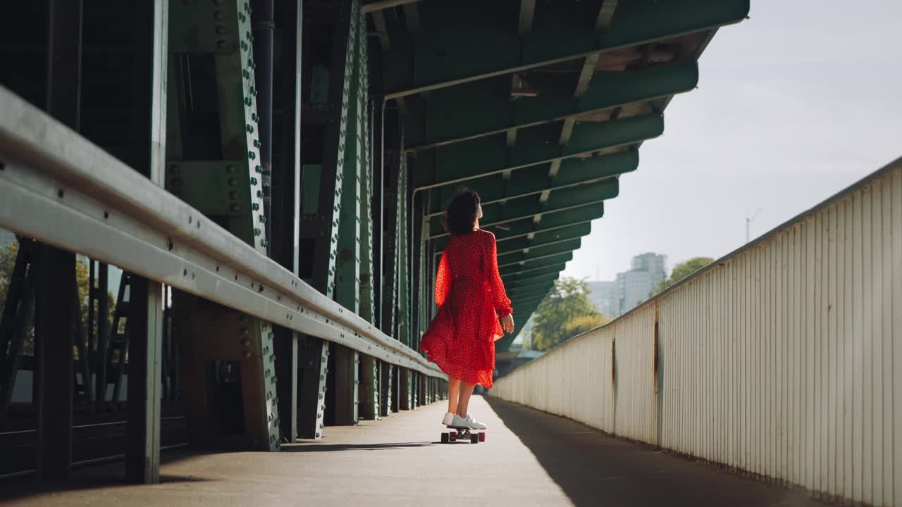 在城市的老火车桥上，穿着红色衣服的女人在玩滑板，女性滑板的城市背景视频下载