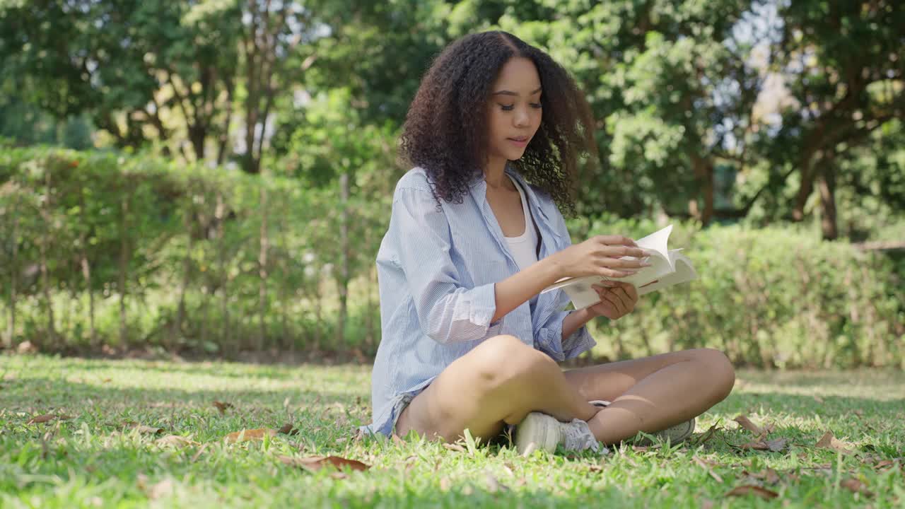 快乐的年轻亚洲女性在周末的空闲时间里，坐在国家绿色公园的草地上，一边看书，一边放松，呼吸新鲜空气，感到快乐。穿着休闲布的女人用爱在大自然中享受片刻，实现保护自然。视频素材