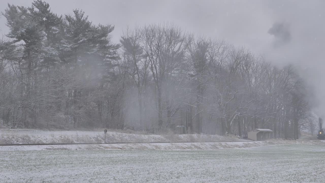 蒸汽火车行驶在白雪覆盖的土地上，它的烟雾与白色的景色形成鲜明的对比。视频下载