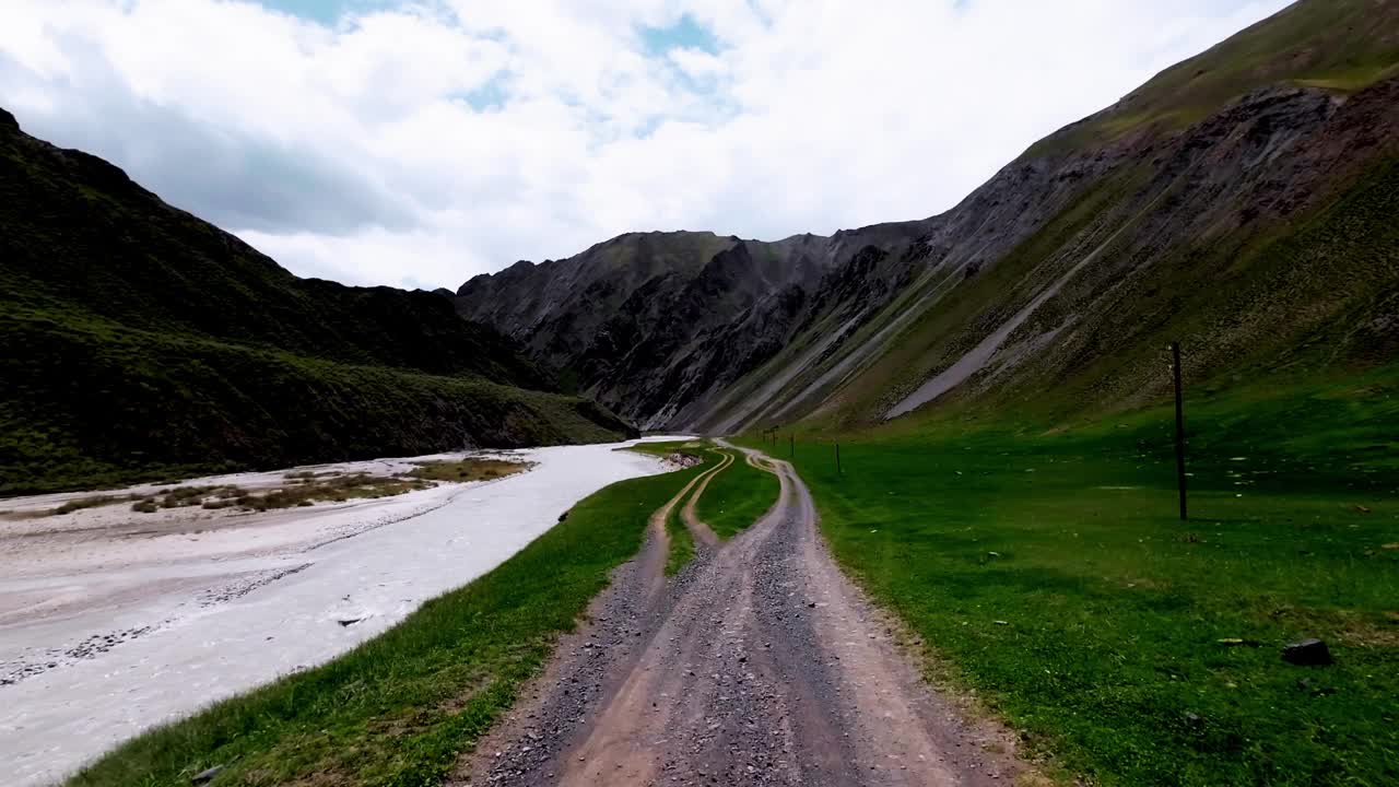 在雨天，宽阔的山间河流在绿色的草地两岸之间。沿河的土路视频素材