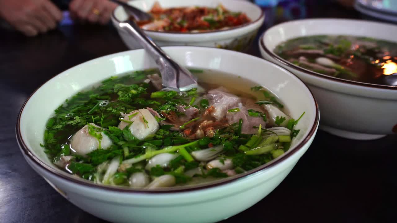 老挝万象当地一家餐馆里，木桌上的白色盘子里摆着老挝式面条，上面放着新鲜蔬菜。视频下载