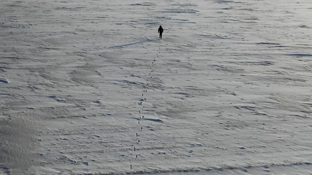 鸟瞰图，一个背着沉重背包的人在阿拉斯加的雪沙漠上行走视频下载