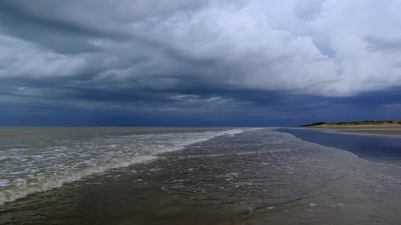 海滩的视频，柔和的海浪，威胁铅灰色的天空和远处的一些沙丘视频下载