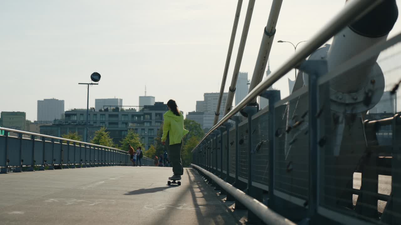 在城市的悬索桥上玩滑板的少女，年轻的女性滑板手，城市背景视频素材