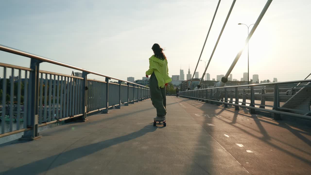 在城市的悬索桥上玩滑板的少女，年轻的女性滑板手，城市背景视频下载