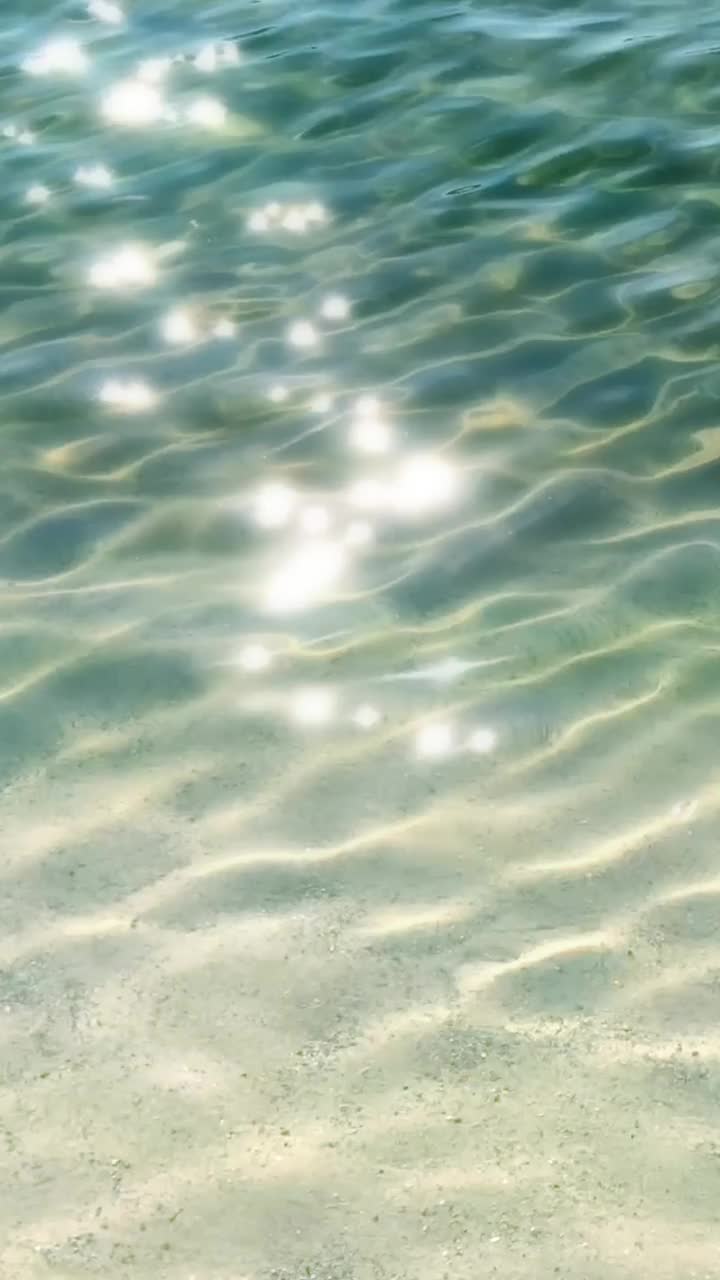 夏日，白色沙滩上的蓝色波纹水面反射着阳光和闪闪发光的灯光，这是海滩度假和旅游胜地的背景视频下载