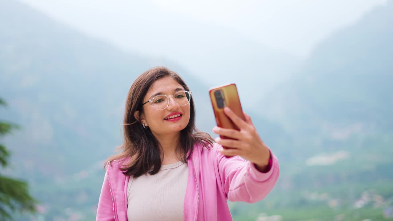 年轻印度女子自拍的4K照片。漂亮的z世代少女视频博主。旅游女孩在印度马纳利山区自拍。女孩穿粉红色的连帽衫。视频素材