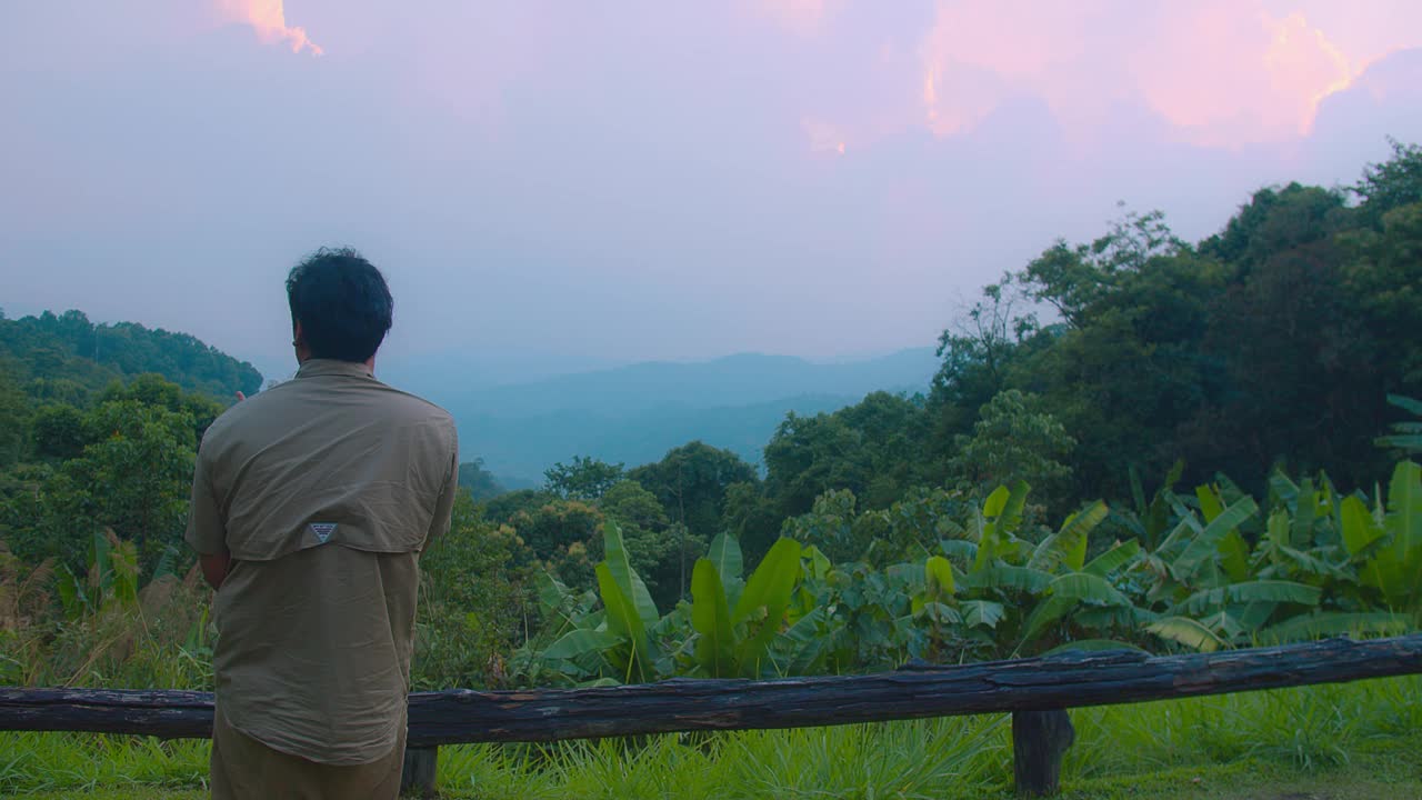 一位父亲带着他的孩子在他的肩膀上欣赏着美丽的山景，夕阳环绕着郁郁葱葱的绿色植物视频素材