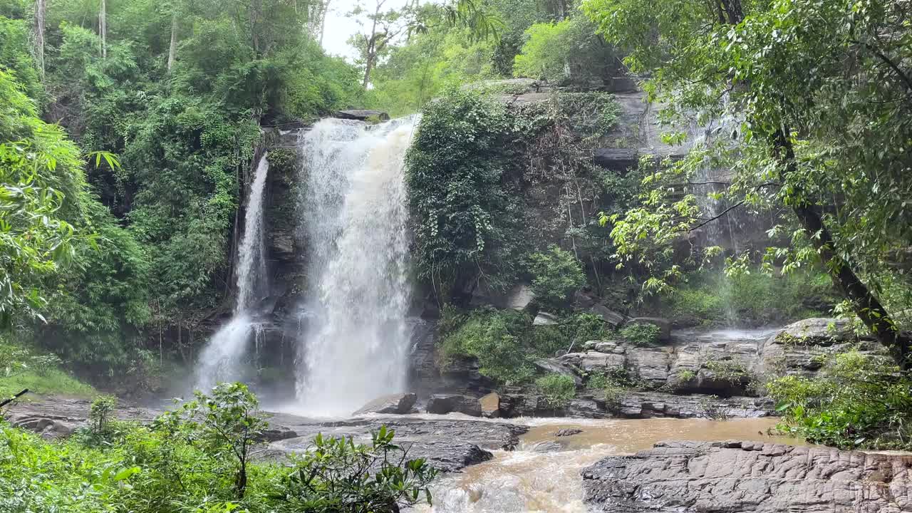 宁静的瀑布坐落在郁郁葱葱的绿色森林中，周围是树木和岩石。视频素材