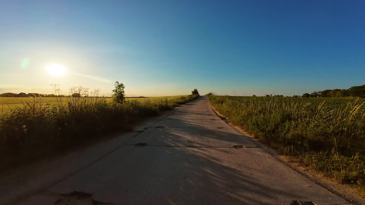 在夕阳下的农道上开车。驾驶员视角的旅程通过独特的景观视频下载