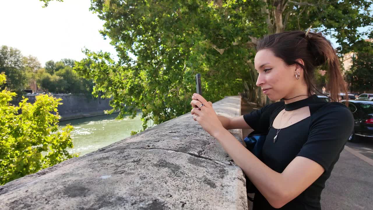 罗马年轻女子在河边用智能手机拍照视频下载