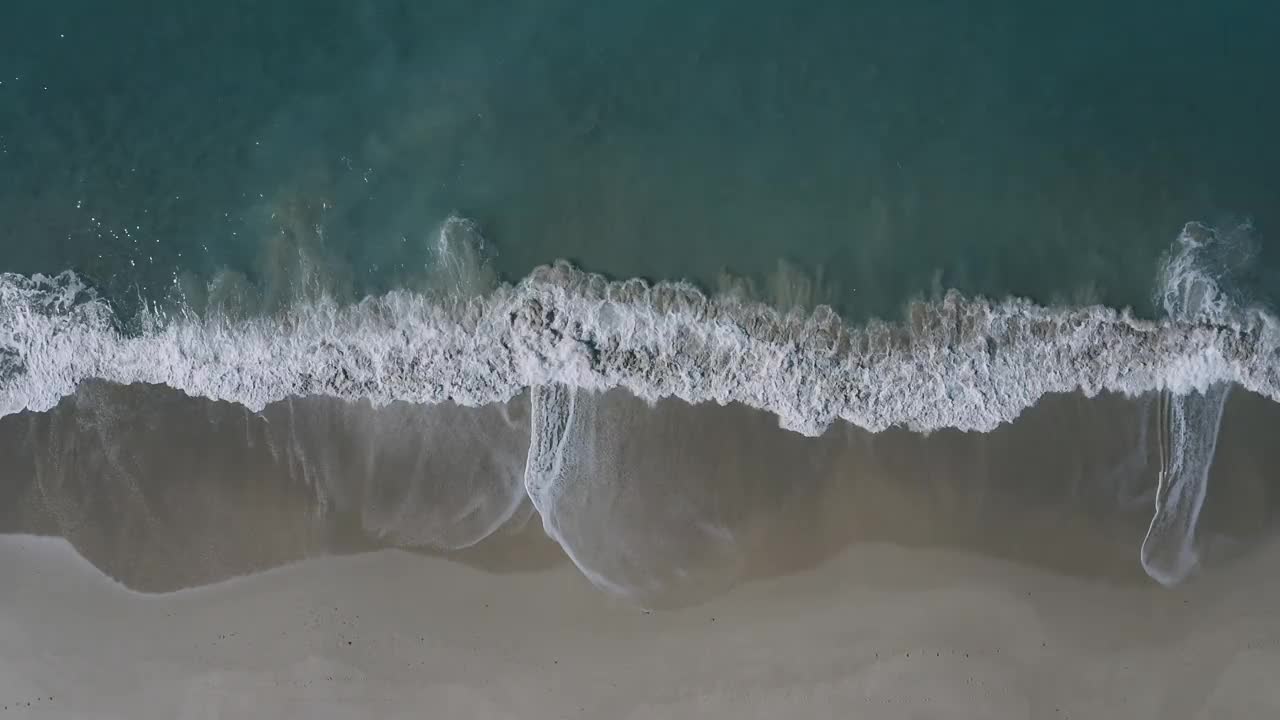 多个波浪沿着浅沙海岸线破碎，创造出抽象的移动纹理。视频素材