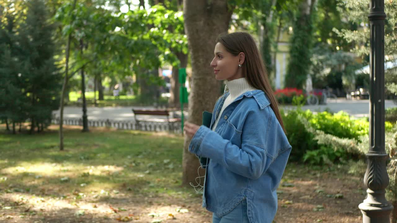 带着平板电脑的女子在户外散步时戴着耳机。摄像机跟踪视频下载