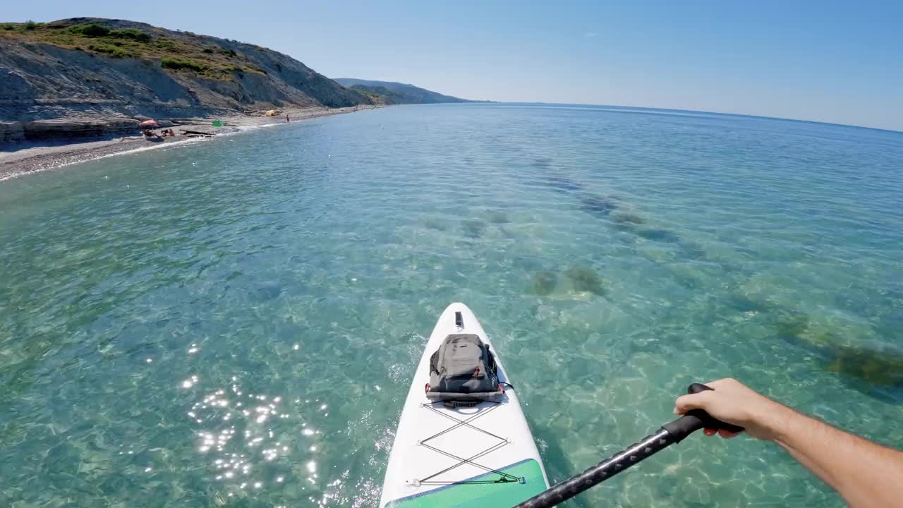 人们在平静透明的海面上划桨。夏季站立桨板的第一人称视角。视频素材