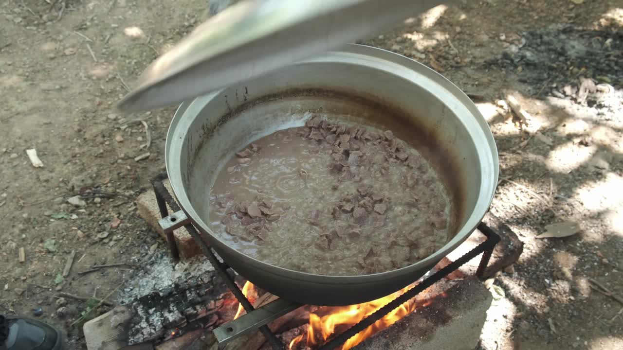 在柴火上烹调烤肉。男人搅拌煮肉检查视频下载