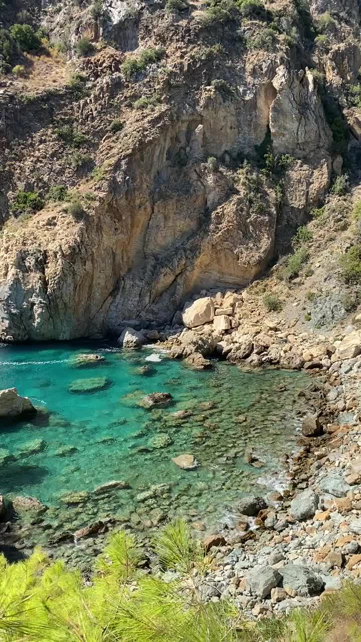 一个岩石悬崖占据了整个景色，从一个小海湾的碧绿海水中陡然升起。视频下载