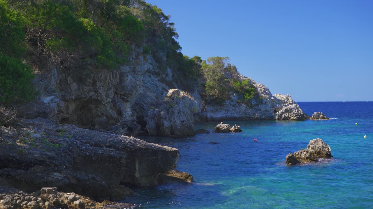 相当平静清澈的绿色大海在岩石海滩岸边，阳光照射到小波浪，典型的风景在利亚帕德斯，希腊的许多海湾之一视频下载