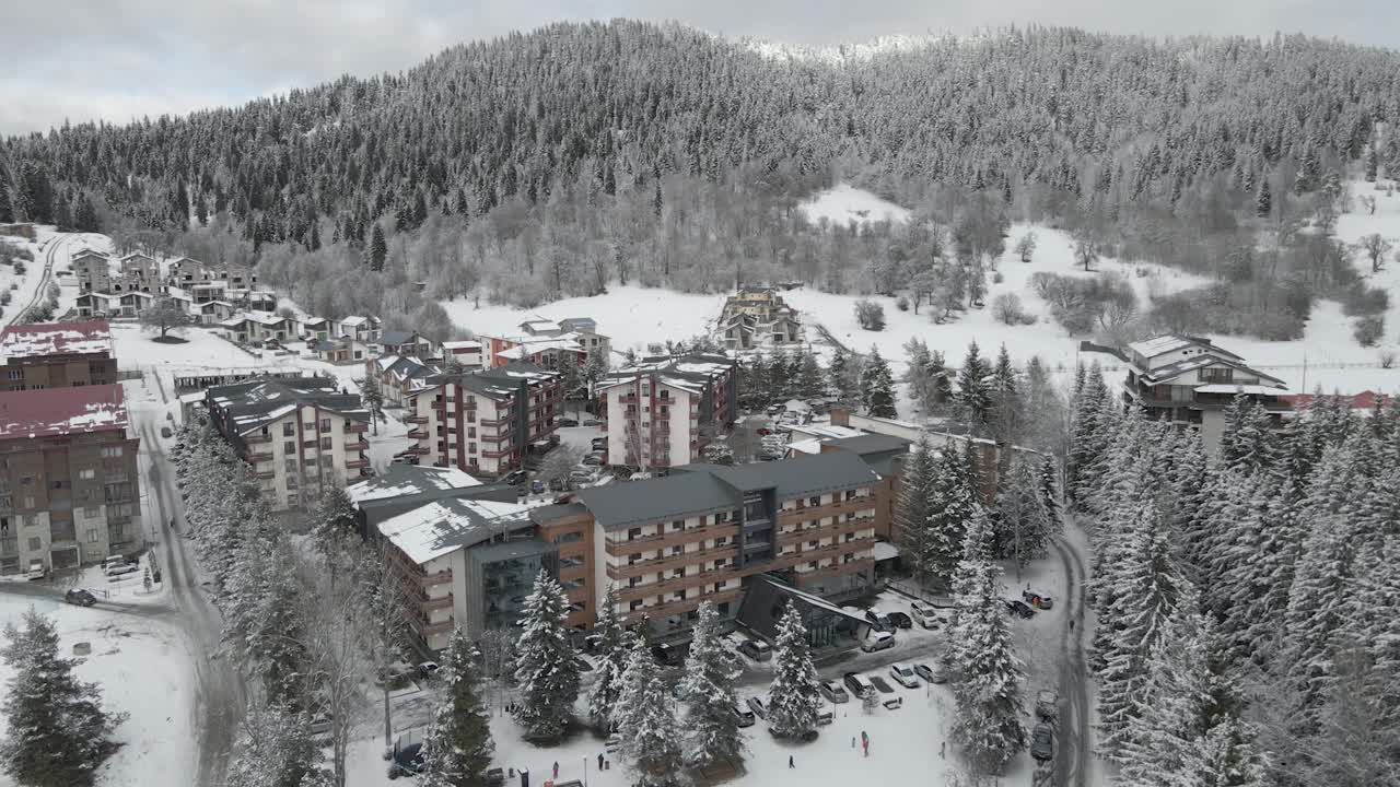 一个迷人的滑雪度假村坐落在白雪皑皑的树木和山脉，提供一个舒适的冬季逃生视频素材