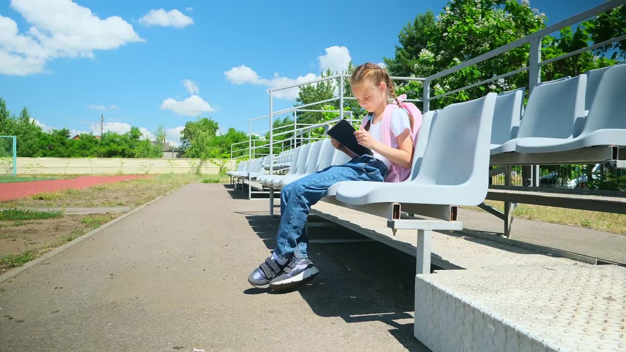 回到学校。小学生。一年级生。开始上课了。一个背着书包的小女孩坐在长凳上，手里拿着课本。视频素材