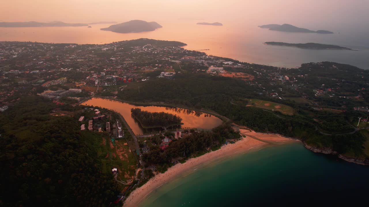 这张风景优美的鸟瞰图展示了日落时的海岸海滩，周围环绕着山丘和岛屿，泰国普吉岛奈汉海滩视频素材